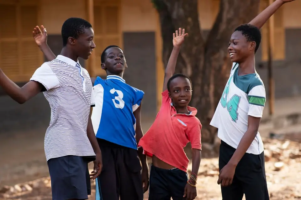 Four children smiling and raising their arms outdoors